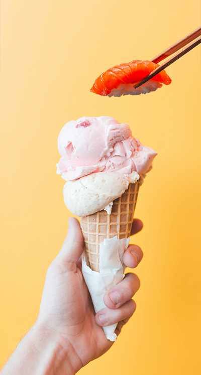 A piece of nigiri held by chopsticks being lowered down onto an ice cream cone.