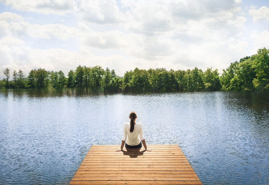 A woman sitting on a dock overlooking a peaceful lake.