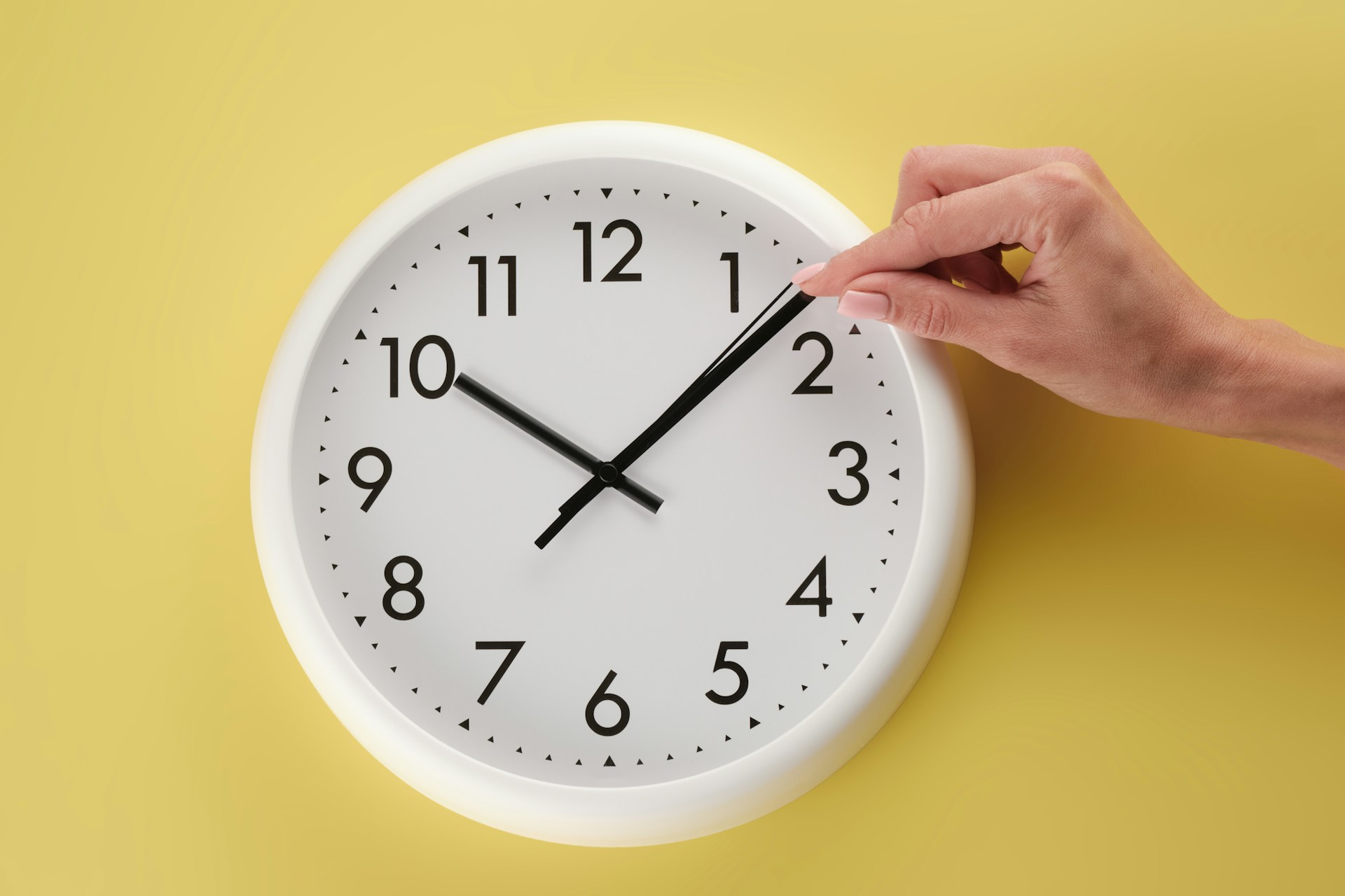 A wall clock with a human hand manipulating the minute hand.